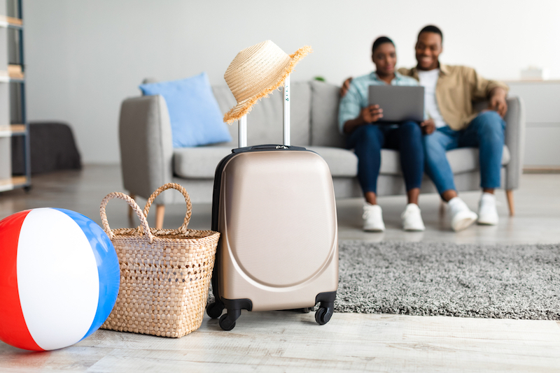 Family Using Laptop While Packed Suitcase And Bags On Floor in Second Home