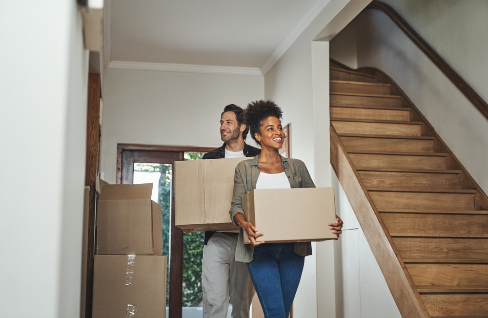 Couple carries moving boxes into new home covered by insurance.