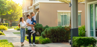 Asian parents hold their young daughter who is pointing to their home.