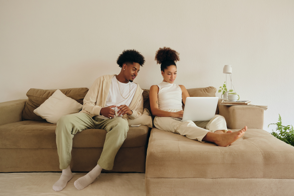 African American couple sit on couch in their home and research home insurance industry terms on a laptop.