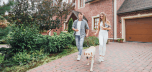Young homeowner couple takes their dog on a walk and discusses market value vs. replacement cost value of their brick home.