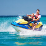 Happy father and son wear life jackets while riding on Jet Ski covered by personal watercraft insurance through Matic.