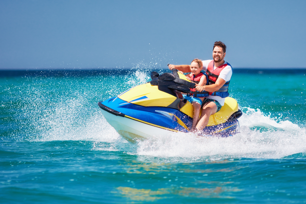 Happy father and son wear life jackets while riding on Jet Ski covered by personal watercraft insurance through Matic.