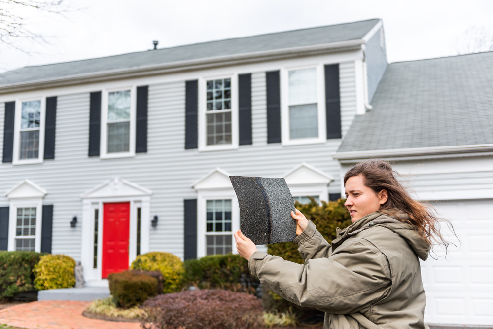 Female homeowner inspects shingle damaged in storm to consider insurance claim.