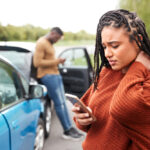 Black female motorist involved in a car accident checks her auto insurance policy with Matic on her phone.