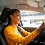 Joyful young African American woman drives car covered by auto insurance in her state.
