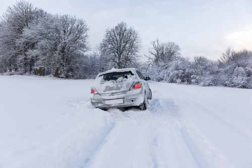 Gray car crashed on side of heavily-covered snowy road.