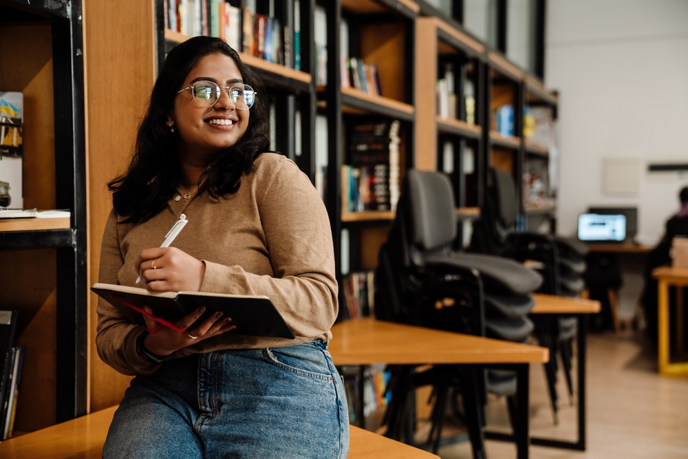 Indian or Middle Eastern college student covered by her parents' homeowners insurance studies in a university library.