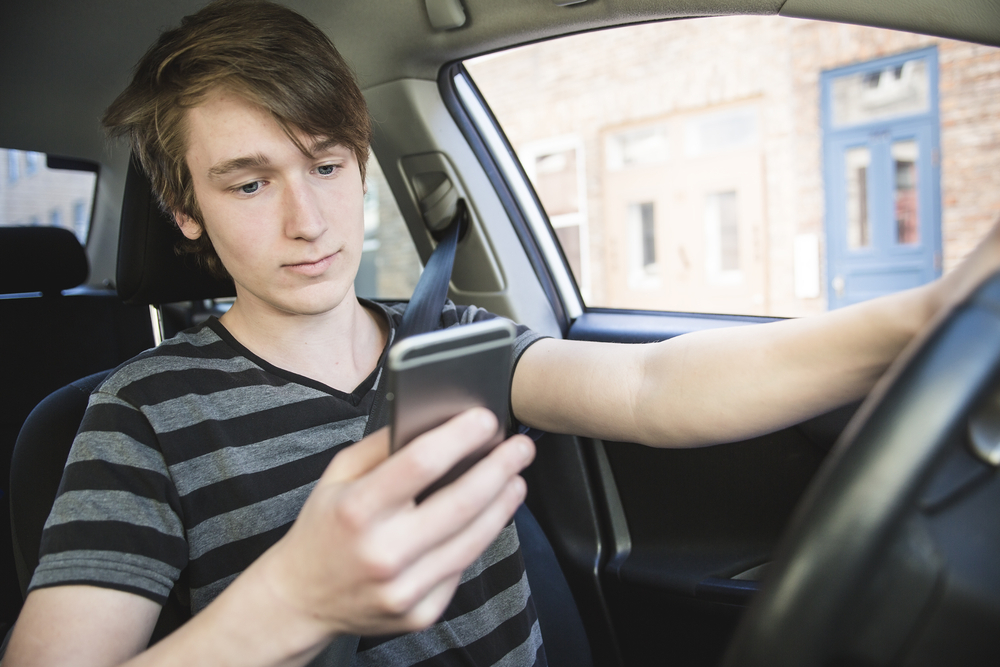 Male teenager showcasing distracted driving by looking at his cell phone.