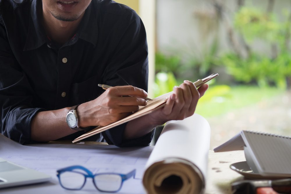 Person writing on a tablet looking at house plans