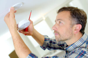 Man wearing plaid shirt installs a smoke alarm in his home.