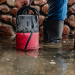 Man wears wading boots as he attempts to clean up water damage covered by his water backup insurance policy that was caused by a sump pump overflow.